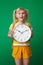 Surprised school girl showing clock isolated on green