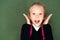 surprised schoolgirl looking at camera while standing near green chalkboard.