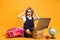 Surprised schoolgirl sits behind a stack of books and laptop holds book on head. Kids education