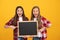 surprised teen girls in casual checkered directing to school blackboard for copy space, offering