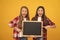 surprised teen girls in casual checkered directing to school blackboard for copy space, offering