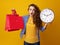 Surprised trendy woman showing clock and red shopping bags