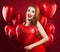 Surprised woman holding balloons red heart, portrait. Girl with red lips makeup wearing red dress. Gift, sale and Valentine`s day