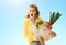 Surprised woman with paper bag with groceries against blue sky