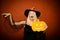 Surprised woman in witches hat and costume on red Halloween background. Pumpkin head jack lantern. Beautiful young