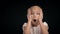 Surprised young girl with open mouth holds head with hands on black background