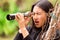 Surprised young woman looking through black monocular in the forest in a blurred background