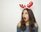 Surprised young woman with reindeer horns on her head looks your pruduct / object with mouth open on gray background. Copy space.