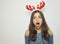 Surprised young woman with reindeer horns on her head with mouth open on white background