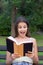 Surprised young woman with widely open yeas and mouth is reading a book outdoors