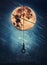 Surreal nightscape with a boy sways on a swing hanging from the full moon. Beautiful starry night with falling comets. Fantasy and