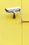 Surveillance camera on the exterior sandwich wall of a yellow building.