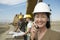 Surveyor in Hardhat In Front Of Heavy Machinery Using Cellphone On Site