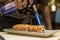 sushi chef preparing maki sushi roll with torch burner, firing direct towards smoke salmon in the kitchen of izakaya