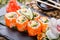 Sushi Roll - Maki Sushi made of Salmon, Red caviar, cucumber, avocado and cream cheese on black stone on bamboo mat decorated with