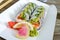 Sushi roll with salmon, avocado, cream cheese, leek, cucumber, tobiko caviar, served on a paper plate.