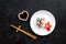 Sushi roll with salmon and avocado on plate with soy sauce, chopstick, wasabi on black background top view