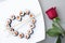 Sushi rolls laid out in the shape of a heart on a white plate. Red rose on a gray background. Creative greetings. The concept of