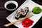 sushi rolls on a white square plate with wasabi, soy sauce and ginger. Dark wooden background