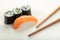 Sushi with salmon and cucumber roll with chopsticks on a light beige background