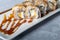 Sushi Sets Nigiri, Uramaki, California, Philadelphia, on a white plate. Nearby ginger and wasabi. Soy sauce in a white bowl. On a
