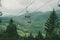 Suspended cable car with open seats, view from top mountain to village located below in valley among coniferous trees