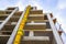 Suspended sections of yellow garbage chute on a facade of building under construction against blue sky with white cloud