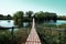 Suspension bridge across the river to the island with deciduous trees. Wooden battens are fastened between the chains.