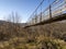 Suspension bridge on iron cables across the autumn valley with a small river