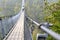 Suspension wooden bridge with steel ropes over a dense forest in West Germany, close-up of a handrail made of rope.