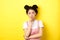 Suspicious asian girl looking at camera and thinking, stare with disbelief, standing with makeup on yellow background