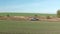 SUV car driving on dirt road on green countryside field, clear skyline background. Aerial side view offroad car