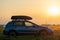 SUV car with roof rack luggage container for off road travelling parked at roadside at sunset. Road trip and getaway concept