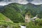 Svan ancient tower in mountain village in Svaneti region of Georgia. Mountains covered green grass. Georgian nature.