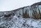 Svartifoss iceland black waterfall completely frozen with bluish stalactites and snow under white sky