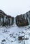 Svartifoss iceland black waterfall completely frozen with bluish stalactites and snow under white sky. Vertical wallpaper