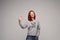 Swag and confident red haired girl in jeans and sweatshirt posing at gray studio.
