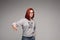 Swag and confident red haired girl in jeans and sweatshirt posing at gray studio.