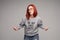 Swag and confident red haired girl in jeans and sweatshirt posing at gray studio.