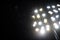 A swarm of mosquitoes and other night insects fly in the light of a stadium reflector near a big river