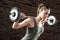 Sweat beautiful girl lifting dumbbells on brick background