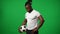 Sweating tattooed footballer with ball standing at chromakey background looking away. African American man playing