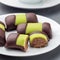 Swedish sweets punch rolls or punschrullar, covered with green marzipan, on a white plate, served with coffee, square format,