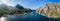 Sweeping drone panorama of Nusfjord, highlighting the serene blue fjord flanked by steep mountains, with the village of Nusfjord