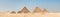 Sweeping panorama of the entire desert and all three of the Great Pyramids at Giza, Egypt nearby on a blue sky day. Horizontal
