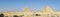 sweeping panorama of the entire desert and all three of the Great Pyramids at Giza, Egypt nearby on a blue sky day. Horizontal