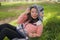 Sweet Asian woman in hoodie making faces - lifestyle portrait of young happy and beautiful Chinese girl sitting playful on green