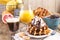 Sweet Belgian waffles for breakfast, decorated with white cream and chocolate sauce. Glass with coffee black and orange juice,