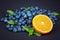 Sweet blueberries with ripe half of orange and green mint. Whole blueberries with half of orange and mint on a dark background.