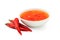 Sweet chilli sauce in a white ceramic bowl next to three red chillies isolated on white